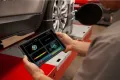 Mechanic using a digital tablet to perform a wheel alignment on a modern vehicle.