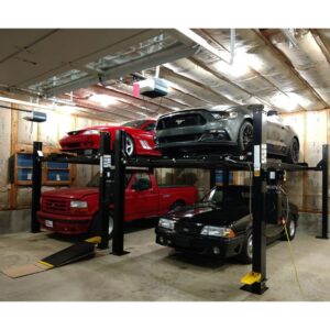 Two cars, a red sports car and a gray Mustang, on a four-post car lift in a residential garage with a red truck and black car parked underneath, showcasing the lift's multi-vehicle stacking capability.