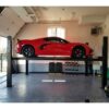 Red sports car elevated on a Direct Lift four-post lift in a clean, organized garage, emphasizing the lift's design and utility for car storage and maintenance.