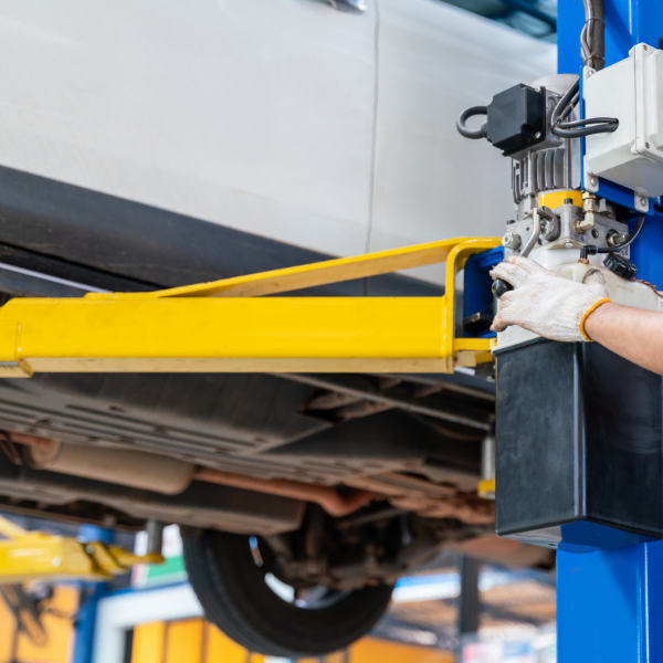 Mechanic operating a two-post car lift control panel with vehicle raised, highlighting risks of cheap car lifts without proper safety features