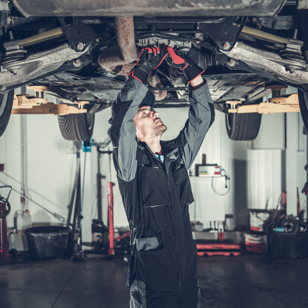Auto technician repairing vehicle underside on a car lift, showing why budget car lifts without certification can be dangerous