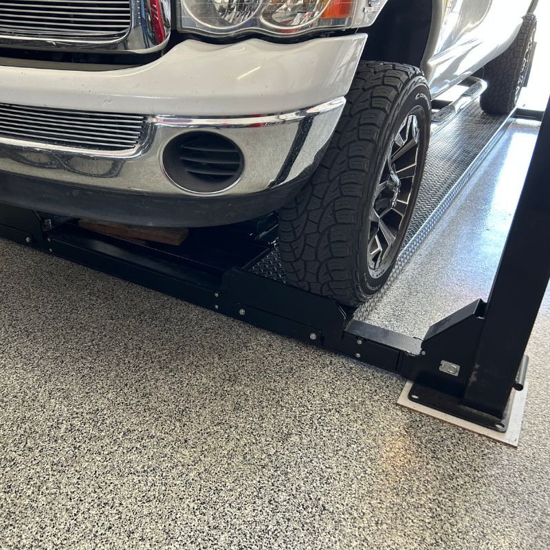 Close-up view of a white Dodge 2500 Quad Cab long-bed truck parked on a PP9P car lift with a focus on the front bumper and wheels.