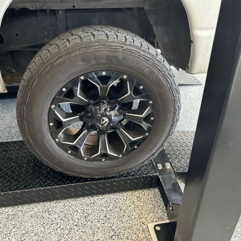 Detailed shot of a black custom wheel and Cooper tire on a white Dodge 2500 Quad Cab long-bed truck on a PP9 car lift.