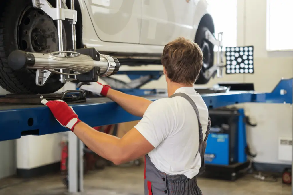 Mechanic performing a wheel alignment on a vehicle using advanced alignment equipment in a workshop.
