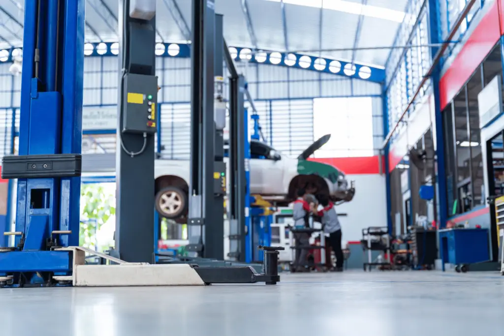 Mechanic working under a lifted vehicle supported by a two-post lift in an auto repair shop.