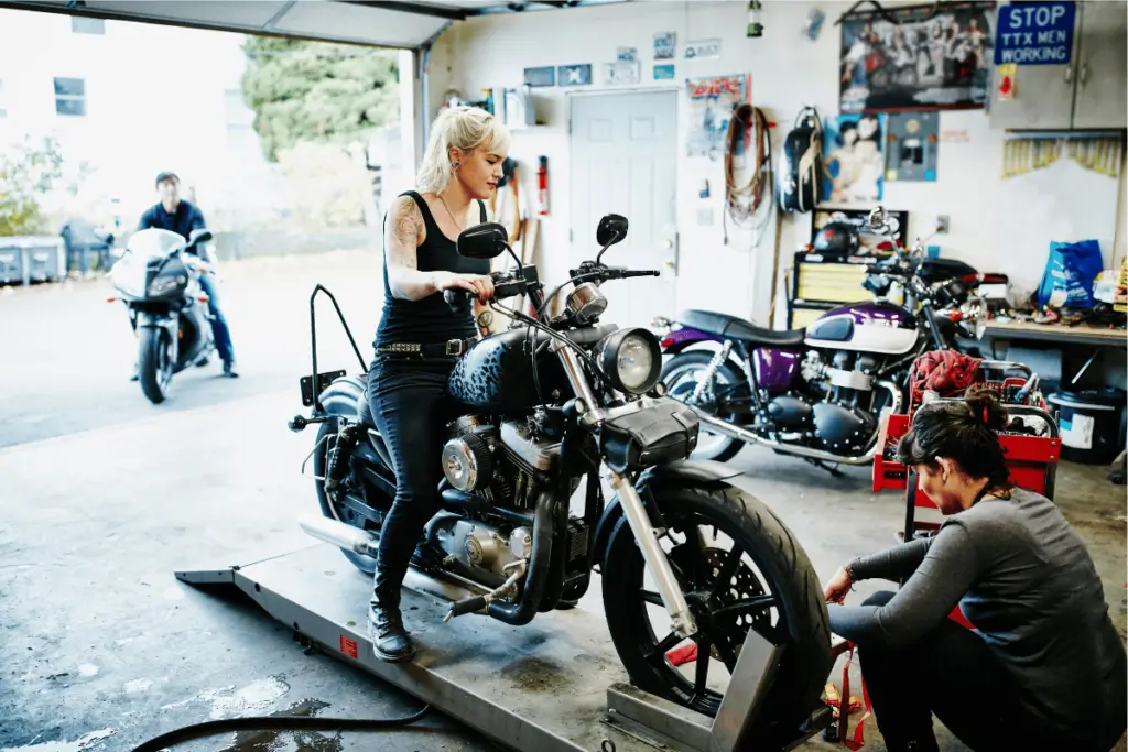 Female motorcycle rider using a lift for servicing her bike in a home garage.