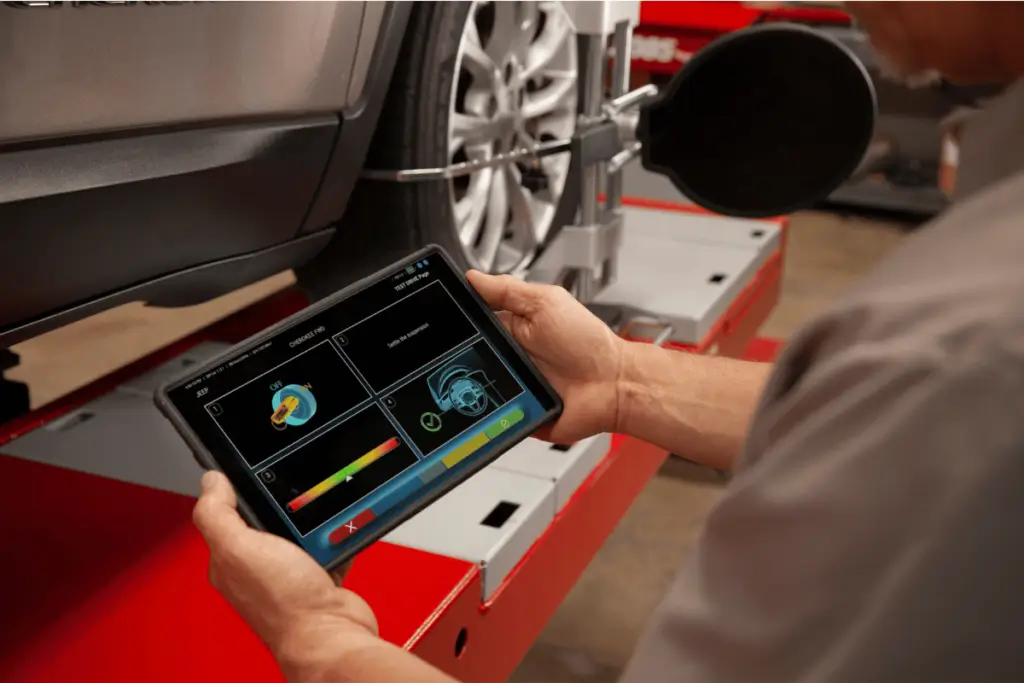 Mechanic using a digital tablet to perform a wheel alignment on a modern vehicle.