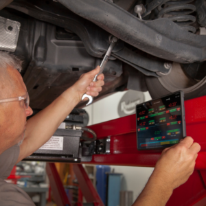 Technician using the Rotary R1085 Pro 3D Wheel Aligner tablet while making suspension adjustments under a vehicle, ensuring precision in real-time alignment.