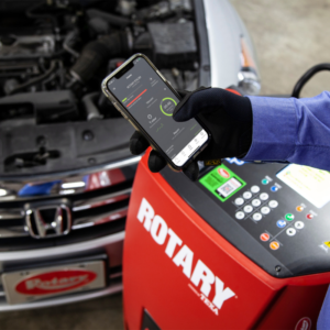 Technician using the Rotary R3AC50 Automatic A/C Cart mobile app for remote control and real-time diagnostics during vehicle A/C servicing.