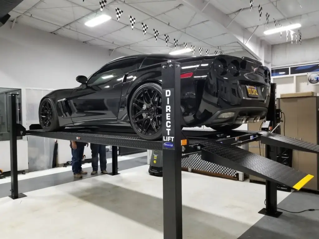 Black Corvette C6 Z06 on a Direct Lift PP8S four-post lift with rear ramps extended in an indoor automotive shop