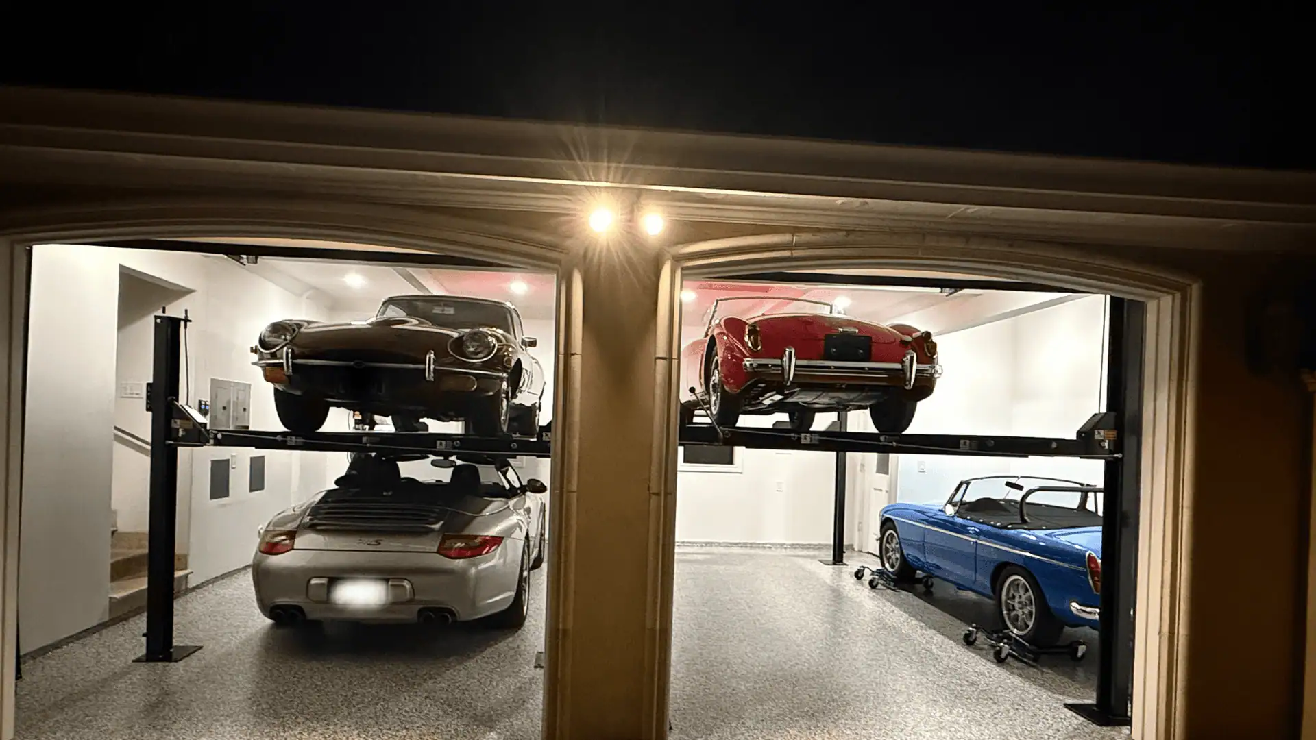 Gallery Residential garage with two Direct-Lift four-post car lifts storing classic sports cars, including a red convertible and silver Porsche, showcasing efficient home car lift storage setup.