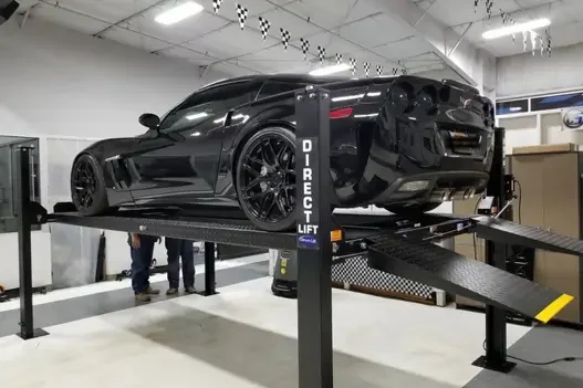 Black sports car on Direct Lift 4-post lift inside a professional garage
