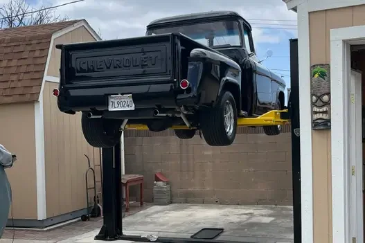 Classic black Chevrolet pickup elevated on a yellow-arm 2-post lift outdoors