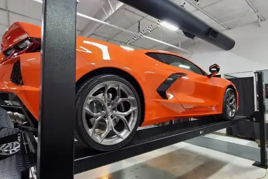 Orange Corvette raised on a 4-post lift in a well-lit automotive workshop
