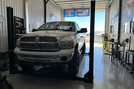 Silver Dodge Ram 1500 truck lifted on a 4-post car lift in a commercial shop
