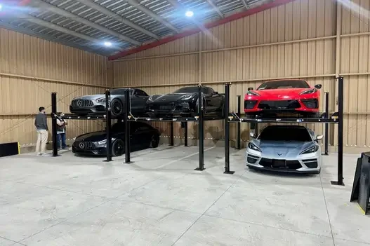 Luxury sports cars including Corvette and Mercedes-Benz on stacked car lifts in a large storage facility