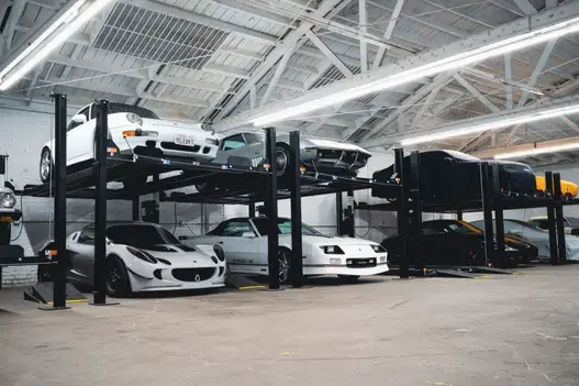White Lotus, Camaro, and Porsche vehicles on 4-post lifts in a spacious industrial warehouse