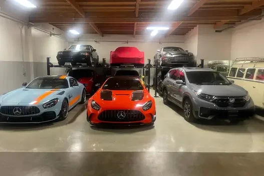 Assorted high-performance and luxury vehicles including AMG and Honda stored with vertical lifts